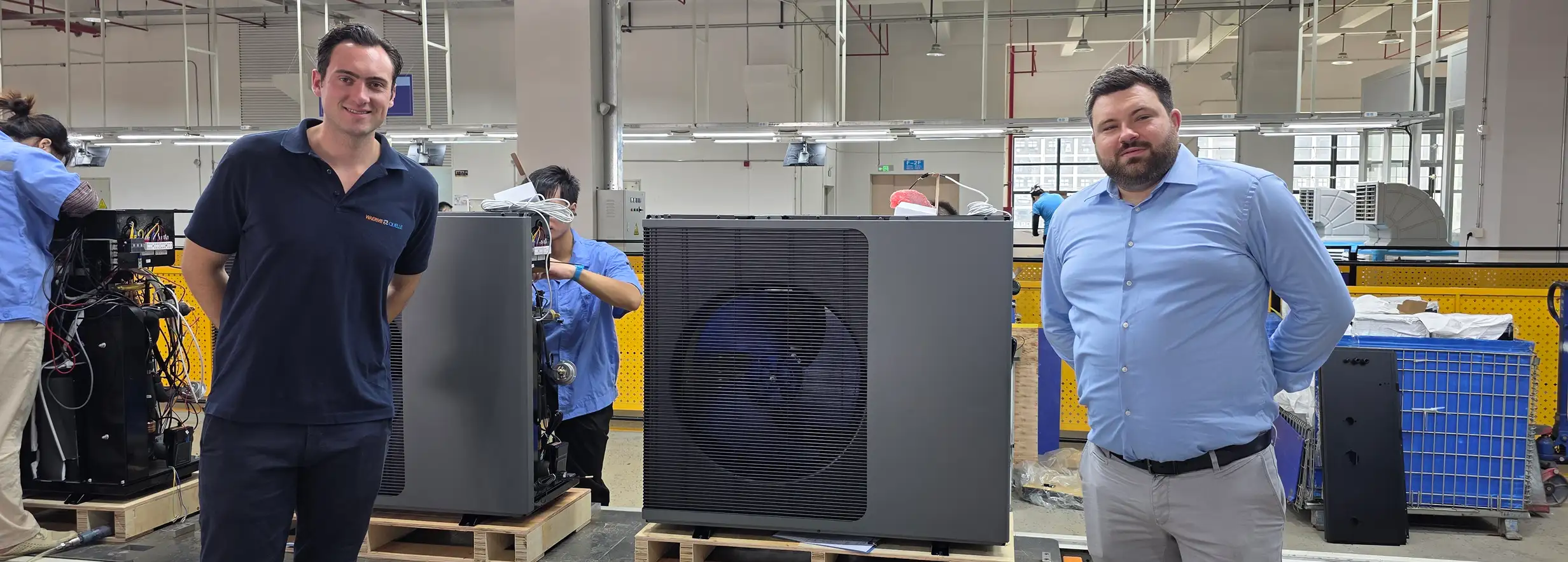 Die beiden Geschäftsführer der Waermequelle GmbH in einer Produktionshalle vor mehreren Wärmepumpen.