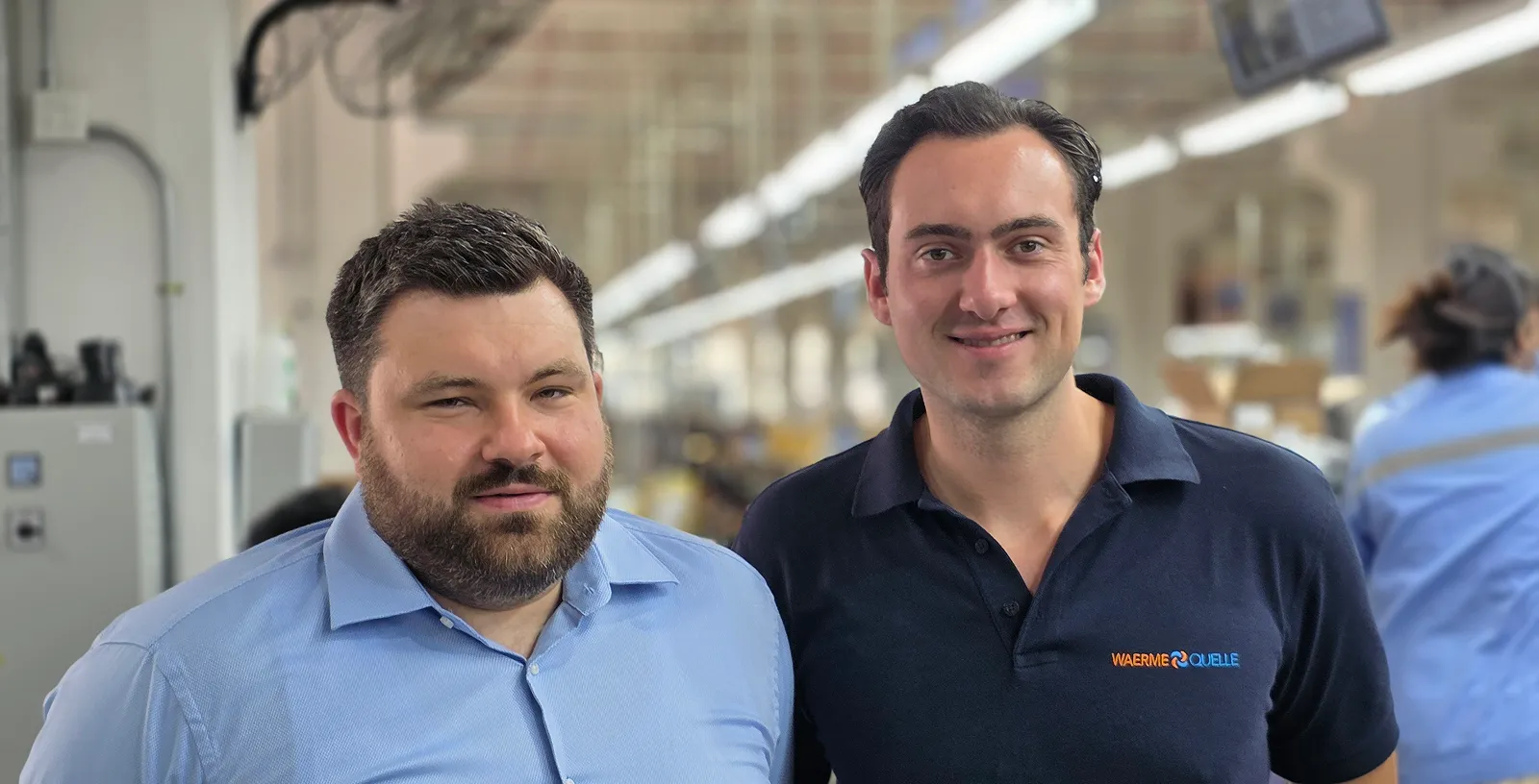 Die beiden Geschäftsführer der Waermequelle GmbH lächelnd in einer Produktionshalle.