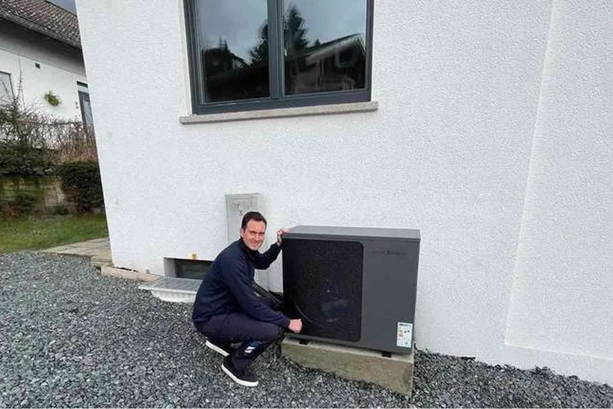 Geschäftsführer der Waermequelle GmbH, Youri Kissner, neben einer Wärmepumpe vor einem Haus kniend.