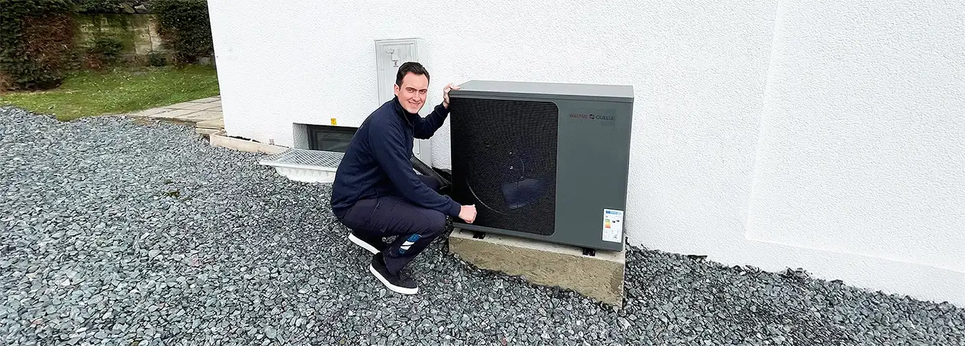 Geschäftsführer der Waermequelle GmbH, Youri Kissner, neben einer Wärmepumpe vor einem Haus kniend.