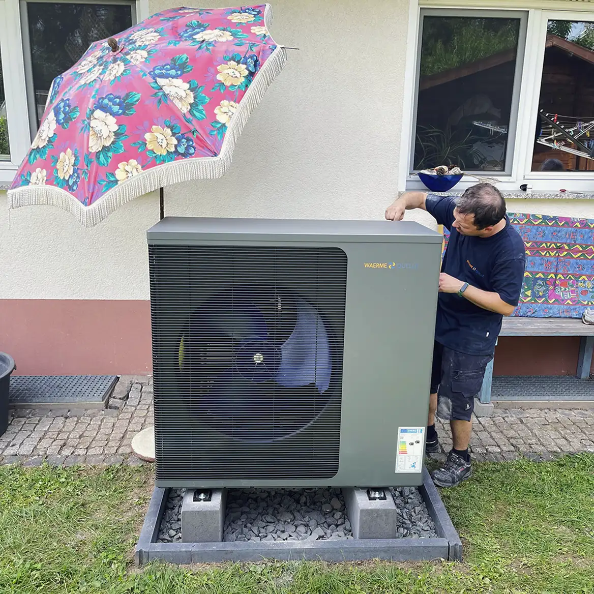 Ein Mitarbeiter des Waermequelle Teams beim Einbau einer Wärmepumpe im Garten vor einem Haus.