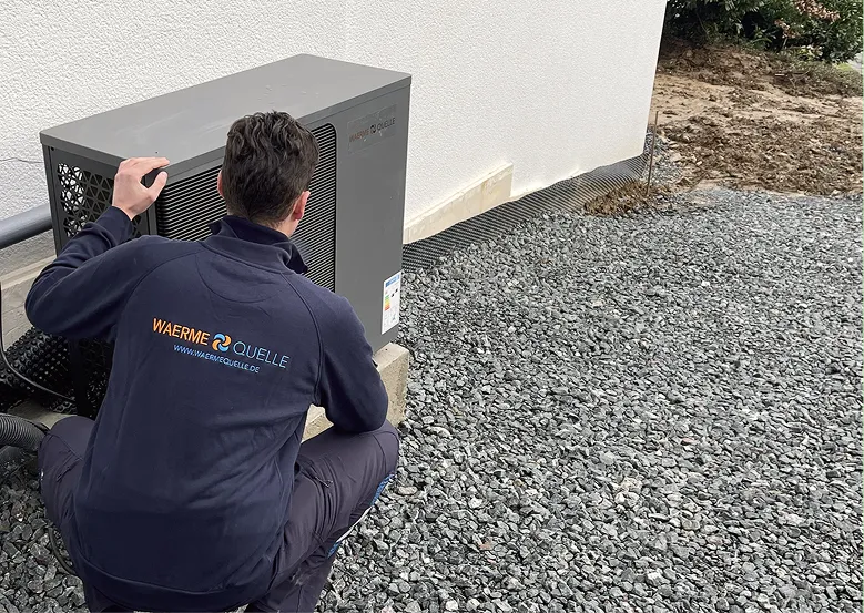 Youri Kissner, Geschäftsführer der Waermequelle GmbH, hockend neben einer Wärmepumpe vor einem Haus.