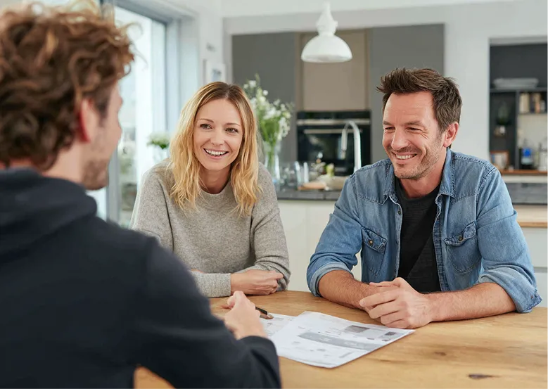 Ein Paar am Tisch in einem Wohnzimmer im Gespräch mit einem Waermequelle Mitarbeiter.