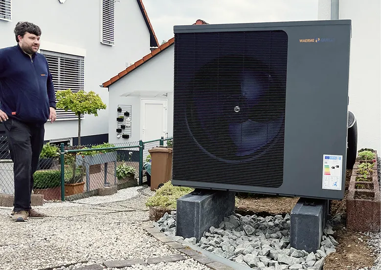 Eine Wärmepumpe der Firma Waermequelle auf Steinen neben einem Haus.