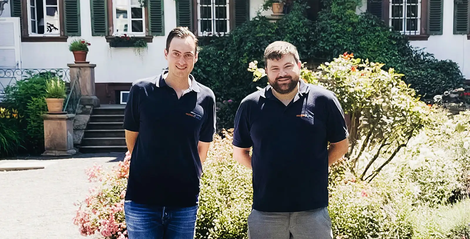 Die Geschäftsführer der Waermequelle GmbH, Youri Kissner und Felix Cvecko, vor einem grünen Busch.