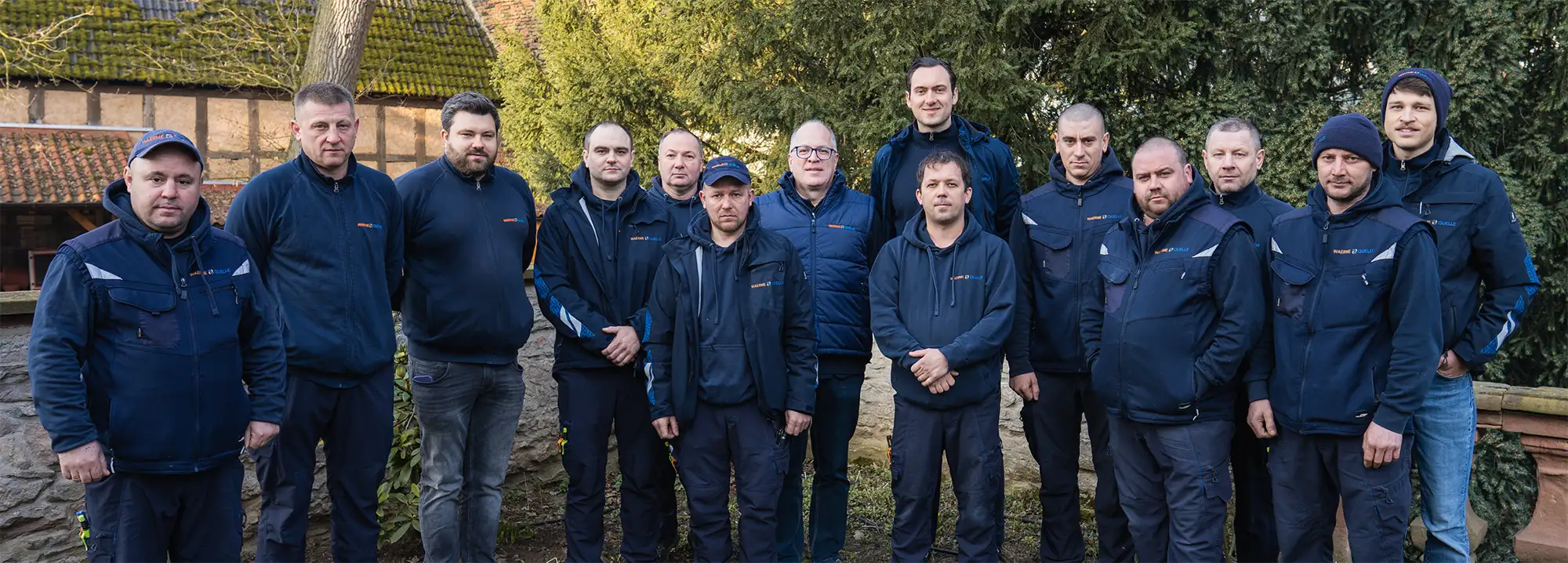 Gruppenbild des Teams der Waermequelle GmbH in dunkelblauer Arbeitskleidung in einem Garten.