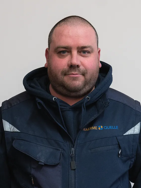 Porträt eines Mitarbeiters der Waermequelle GmbH mit dunkelblauer Jacke mit Waermequelle Logo.