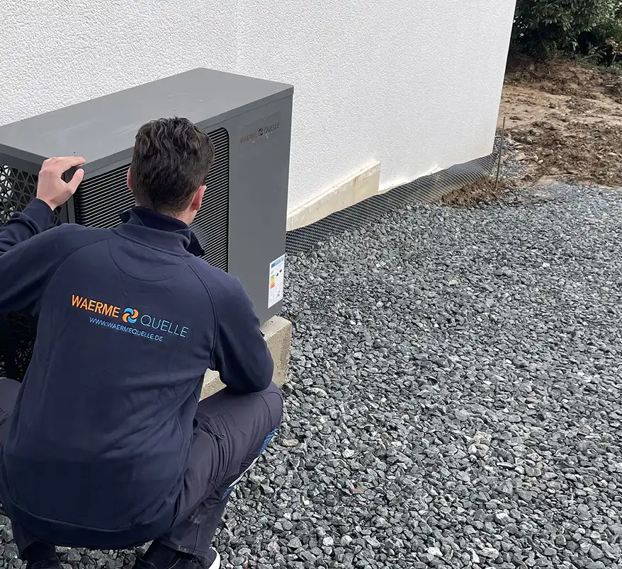 Youri Kissner, Geschäftsführer der Waermequelle GmbH, hockend neben einer Wärmepumpe vor einem Haus.