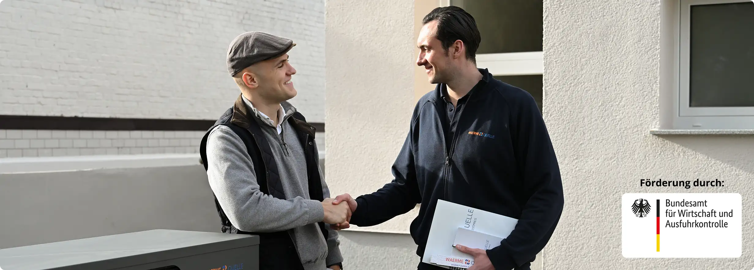 Geschäftsführer der Waermequelle GmbH, Youri Kissner, schüttelt einem Kunden vor einer Wärmepumpe die Hand.